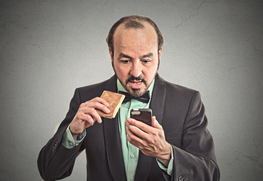 surprised business man eating on a go cookie using smartphone