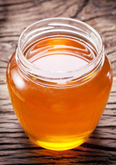 Glass can full of honey on wooden table.