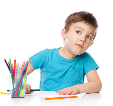 Cute boy is drawing using color pencils