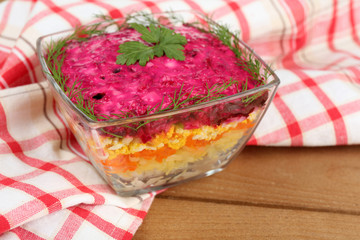 Russian herring salad in glass bowl on wooden table background