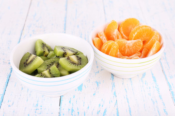 Bowls of slices kiwi and mandarin on color wooden background