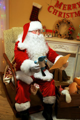 Santa Claus sitting with list of presents in comfortable chair