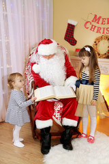 Santa Claus reading book with two little cute girls near