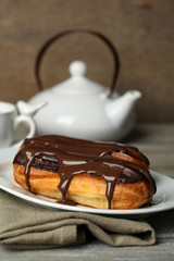 Tasty eclairs and pot of tea on wooden table