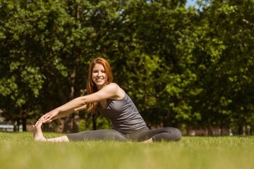 Naklejka na ściany i meble Pretty redhead smiling stretching in park