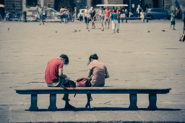 Young couple sitting in a bench in Santa Croce square, Florence,