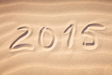 Fototapeta na wymiar 2015 handwriting on the sea-sand with a wavy pattern