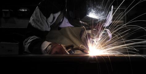 Employee welding steel using MIG/MAG welder. - obrazy, fototapety, plakaty
