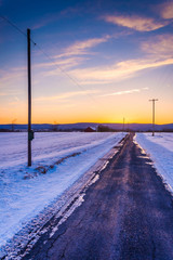 Fototapeta na wymiar Sunset over a country road through snow covered fields in rural