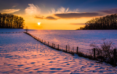 Sunset over a fence in a snow covered farm field in rural Carrol - Powered by Adobe
