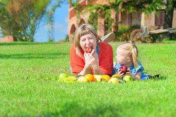 Naklejka na ściany i meble Mother and daughter eating the colorful fruit on green grass