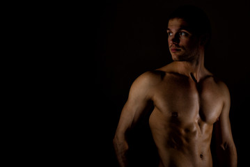 Fototapeta na wymiar Muscular male model on black background. Place for your text.