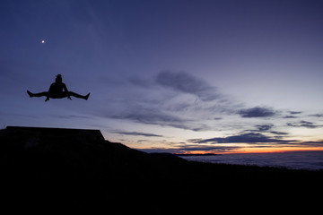 silhouetted gymnast doing the splits jump after sunset