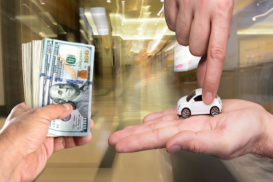 One man holding dollar banknotes, another man holding small car