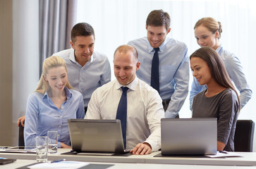 smiling businesspeople with laptops in office