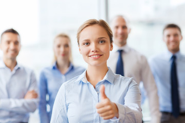 Fototapeta na wymiar smiling businesswoman showing thumbs up in office