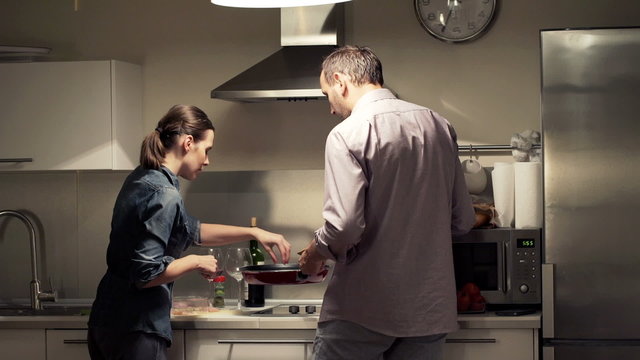 Young Couple Cooking, Putting Meat On Pan And Talking In Kitchen