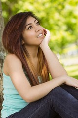 Fototapeta premium Beautiful woman sitting against tree in park
