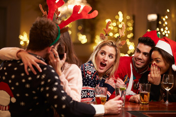 Obraz na płótnie Canvas Couple Kissing In Bar As Friends Enjoy Christmas Drinks
