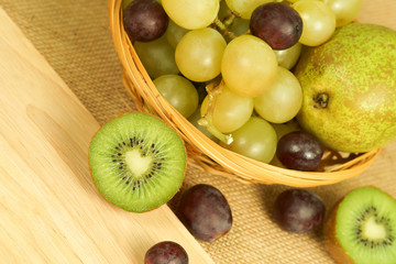 Cutted green kiwi on the board and fruits basket