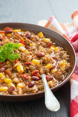 Mexican dish chili con carne in a brown pottery plate, vertical