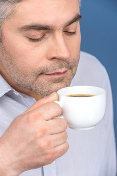 Happy adult man drinking coffee on blue.