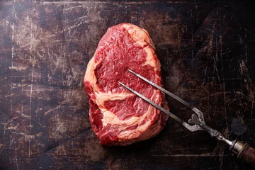 Crédence de cuisine en verre imprimé Viande Viande fraîche crue Ribeye Steak et fourchette à viande sur fond sombre