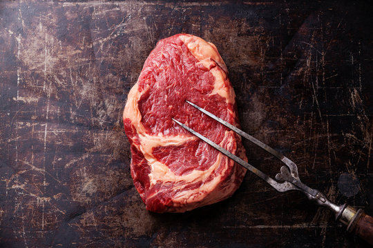 Raw fresh meat Ribeye Steak and meat fork on dark background
