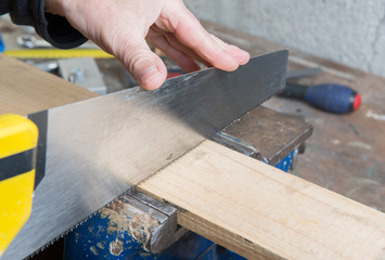 a worker cut a plank of wood with a hand saw