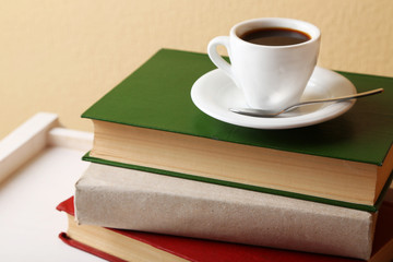 Pile of books with cup on tabletop and light wall background