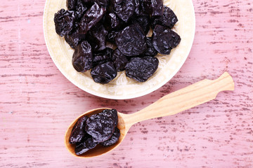 Bowl and spoon of prunes on color wooden background