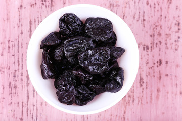 Bowl with heap of prunes on color wooden background