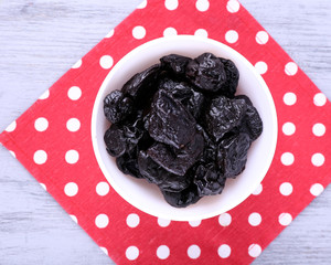 Bowl of prunes on polka-dot napkin on color wooden background
