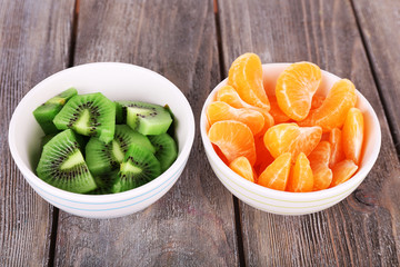 Bowls of slices kiwi and mandarin on rustic wooden background