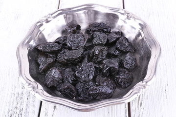 Metal plate of prunes on color wooden background