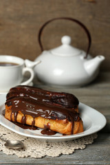 Tasty eclairs and cup of tea on wooden table