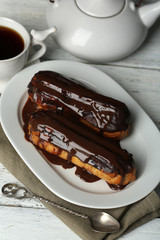 Tasty eclairs and cup of tea on wooden table