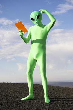 Confused Green Alien Man Scratching Head Holding Tablet