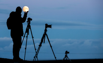 Backlit of photographers with tripod and cameras on full moon