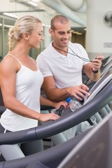 Male trainer timing his client on treadmill at gym