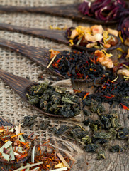 assortment of dry tea in spoons on wooden surface