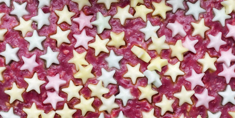 Colorful edible stars in red cream. Background. Photo.