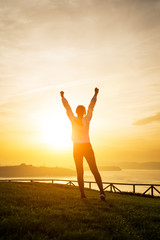 Happy female athlete raising arms towards the sun