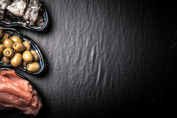 Fish assortment and olives on a plate on a dark background. With