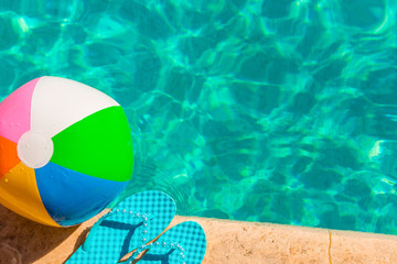Obraz premium turquoise flip flops and ball on the edge of the pool