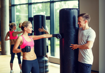 smiling woman with personal trainer boxing in gym