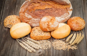 Brotlaib mit Brötchen und Getreideähren auf Holztisch