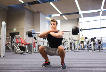 Naklejka na ściany i meble young man flexing muscles with barbell in gym