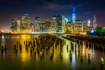 Pier pilings and the Manhattan skyline at night, seen from Brook