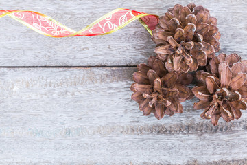 Pine cones and red ribbon on wood background